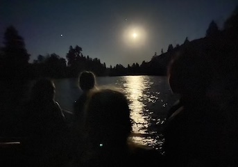 The moon reflects off the yakima river at night and the outlines of people are visible in the foreground.