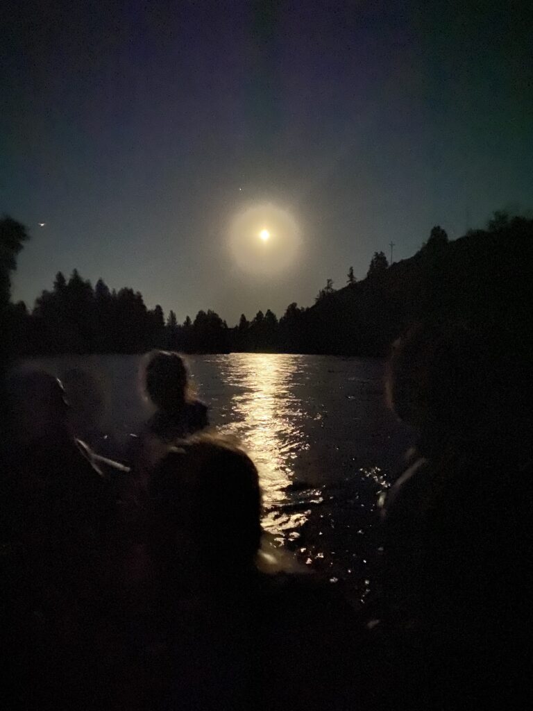The moon reflects of the Yakima River and the outlines of people can be visible in the foreground.