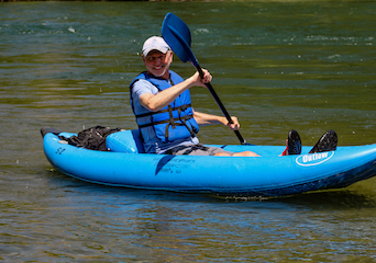 A smiling man learns how to navigate a blue kayak on the Yakima River.